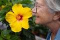 Closeup on senior caucasian woman smelling a yellow hibiscus flower, elderly lady nature lover Royalty Free Stock Photo