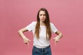 Closeup of serious strict young woman wears white shirt looks stressed and pointing up with finger isolated over pink