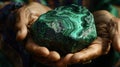 A closeup of a shamans hands cupping a large piece of tumbled malachite. The rich green color seems to pulsate with