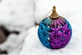 Closeup of shiny Christmas ball colored in purple and blue on a white snow outdoor with copy space on the left