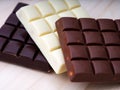 A closeup short of three chocolate bars - milk chocolate, dark chocolate and white chocolate on a wooden background