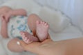 Closeup shot of an adult holding the feet of a little child lying on the bed under the lights Royalty Free Stock Photo