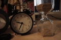 Closeup shot of an alarm clock and a sandglass on the table