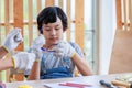 Closeup shot of Asian young boy son in jeans bib outfit with gloves wearing safety goggles sitting at working table workbench with Royalty Free Stock Photo