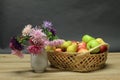 Closeup shot of a basket with assorted fresh fruits with a vase of flowers on a wooden surface Royalty Free Stock Photo