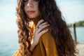 Closeup shot of beautiful young woman with curly hair wearing in yellow sweater sitting on a beach Royalty Free Stock Photo