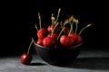 Closeup shot of black bowl full of ripe cherries on gray marble table with black background Royalty Free Stock Photo