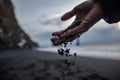Closeup shot of black sand falling between fingers from a hand with a beach in a blurry background. Royalty Free Stock Photo