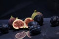 Closeup shot of blue plums, whole figs, and half-sliced figs on a blue surface with a reflection