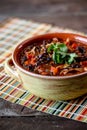 Closeup shot of a bowl of homemade chilli topped with cilantro leaves on a colorful table mat