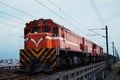 an orange train on the tracks near power lines and trees