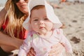 Closeup shot of a Caucasian baby girl sitting with her mother on a sandy beach with blur background