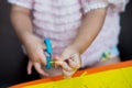 Closeup shot of a child`s hand using blue scissors to carefully cut a small piece of yellow colored paper