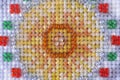 A closeup shot of a cross stitch mades with gray, yellow and gold threads and colour beads