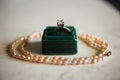 Closeup shot of a diamond ring in a green box on the table with a pearl necklace under the lights Royalty Free Stock Photo