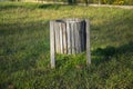 Closeup shot of an empty street garbage wooden bin on a green grass in the park during sunri