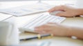 Closeup shot of female hand holding white wireless mouse while working with computer keyboard and chart graph document on office Royalty Free Stock Photo