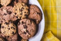 Closeup shot of freshly baked chocolate chip cookies in a white plate on a yellow textile Royalty Free Stock Photo