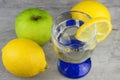 Closeup shot of a glass of lemon juice with a sliced lemon next to whole lemons on a gray surface Royalty Free Stock Photo