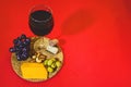 Closeup shot of a glass of red wine, ripe grapes, nuts, green olives, and cheese on a red background Royalty Free Stock Photo