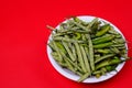 Closeup shot of green beans and chili pepper on plate isolated on red background Royalty Free Stock Photo