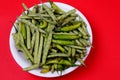 Closeup shot of green beans and chili pepper on plate isolated on red background Royalty Free Stock Photo