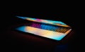 Closeup shot of a half-opened laptop with colorful lights in a dark setting