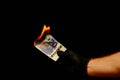Closeup shot of a hand burning money on a dark background
