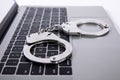 Closeup shot of handcuffs lying on laptop keypad - online crime concept