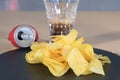 Closeup shot of a heap of delicious potato chips on a black plate with a glass of soda