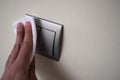 Closeup shot of a human hand cleaning a silver light switch with a wet wipe