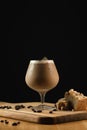 Closeup shot of an ice cappuccino glass on a wooden plate with decorations on a black background