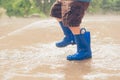 Closeup shot of the legs of a boy in blue rubber boots splashing in a puddle