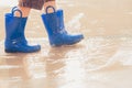 Closeup shot of the legs of a boy in blue rubber boots splashing in a puddle