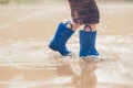 Closeup shot of the legs of a boy in blue rubber boots splashing in a puddle