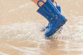 Closeup shot of the legs of a girl in blue rubber boots splashing in a puddle