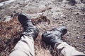 Closeup shot of the legs of the person with black hiking boots on dirt and rocks