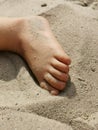 Closeup shot of a little foot in beach sand under the rays of the sun