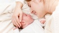 Closeup shot of little newborn baby lying next to mother and crying. Happy smiling woman looking at her little child