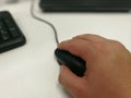 Closeup shot of a male hand holding a computer mouse next to a black keyboard Royalty Free Stock Photo