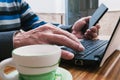 Closeup shot of a male hand using a laptop and a cellular phone with a cup of coffee Royalty Free Stock Photo