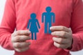 Closeup shot of a male holding two blue people figurine paper cut-outs under the lights