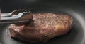 Closeup shot of man hands flip ribeye steak on non stick pan with steel tongs Royalty Free Stock Photo