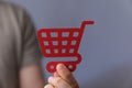 Closeup shot of a man holding a red shopping cart icon on a grey background Royalty Free Stock Photo