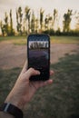 Closeup shot of a man's hand holding a phone and taking pictures of a beautiful summer landscape Royalty Free Stock Photo