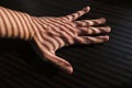 Closeup shot of a man's hand on a table with jalousie shadows