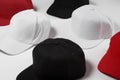 Closeup shot of many baseball snapback hats in different colors black, white and red laid out on white surface