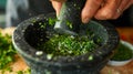 A closeup shot of a mortar and pestle being used to crush fresh herbs