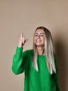 Nice smiling young blonde girl on beige background pointing finger up to draw attention to important information