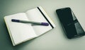 Closeup shot of a notebook with a grey and purple pen on it next to a phone Royalty Free Stock Photo
